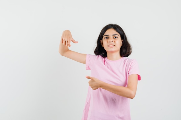 Menina na camiseta rosa mostrando os polegares para cima e para baixo, vista frontal.