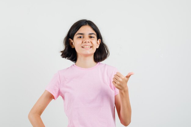 Menina na t-shirt rosa aparecendo o polegar e parecendo jovial, vista frontal.