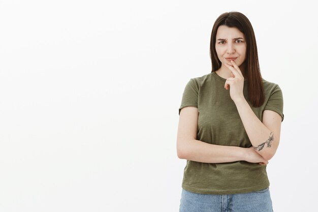 Menina não gosta do que ouve, franzindo a testa e franzindo o nariz de antipatia e confusão, segurando a mão acima do lábio, apertando os olhos e cruzando um braço sobre o corpo, ouvindo sugestões absurdas e decepcionantes