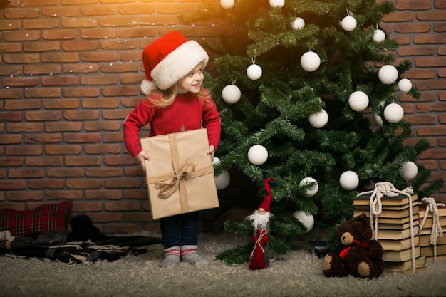Menina no Natal com caixa de presente pela árvore de Natal