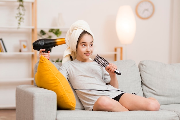 Menina no sofá com secador de cabelo e escova