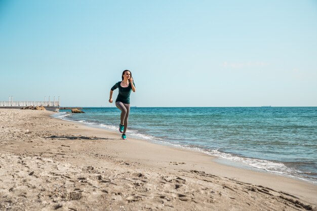 Menina no sportswear correndo ao longo do mar