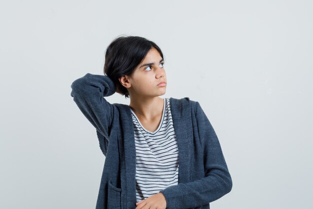 Menina olhando de lado com a mão no pescoço em t-shirt, jaqueta e olhando focado.