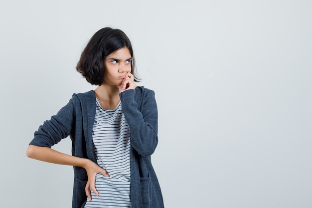 Menina olhando de lado em t-shirt, jaqueta e parecendo hesitante.