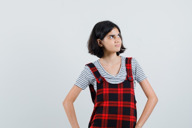 Menina olhando de lado em t-shirt, macacão e olhando focado.