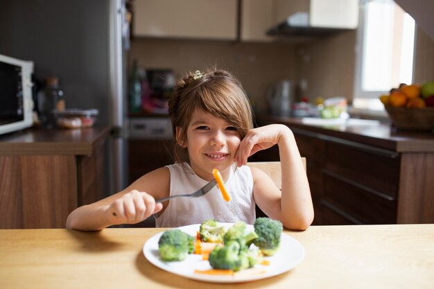 Menina olhando para a câmera enquanto come legumes