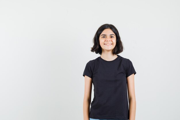 Menina olhando para a frente em uma camiseta preta e parecendo alegre. vista frontal.