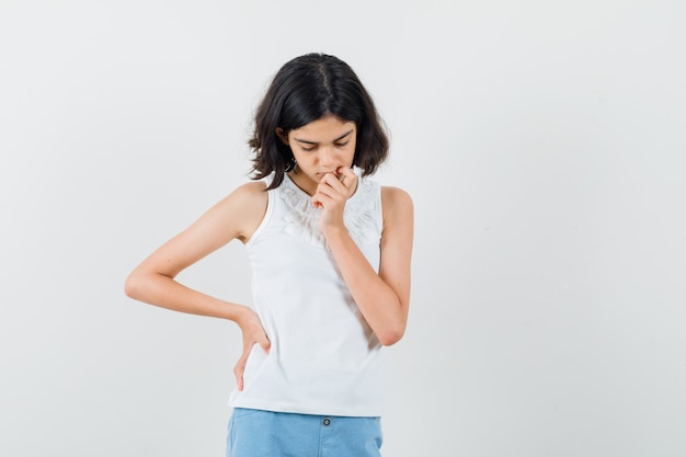 Menina olhando para baixo em blusa branca, shorts e olhando pensativa, vista frontal.