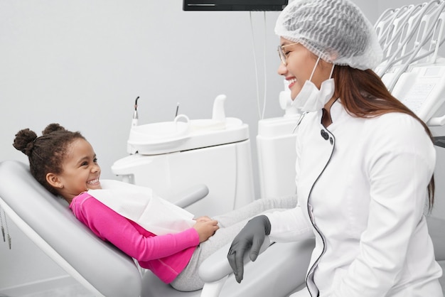 Menina olhando para dentista feminina e rindo na clínica