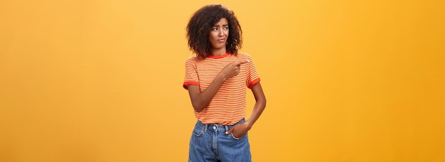 Foto grátis menina olhando para o desempenho inexpressivo duvidoso do modelo retrato de mulher de pele escura confusa e descontente com penteado afro olhando e apontando para a esquerda com desprezo e indiferença