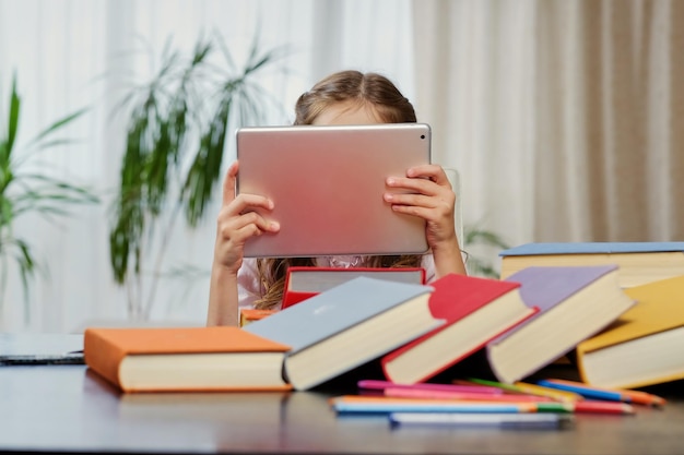 Menina olhando para o tablet pc em uma sala de aula. livros coloridos à mesa.