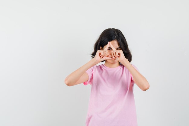 Menina olhando por entre os dedos em uma camiseta rosa e parecendo alegre. vista frontal.