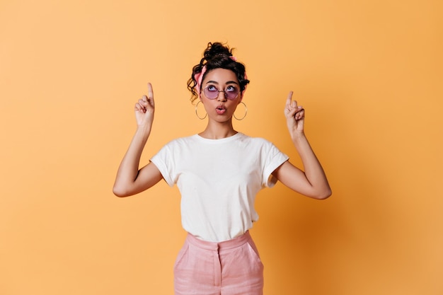 Menina pensativa, apontando com os dedos foto de estúdio de mulher elegante emocional em camiseta branca