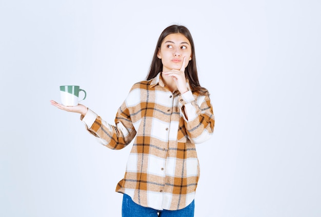 Foto grátis menina pensativa com uma xícara de café em pé e pensando na parede branca.