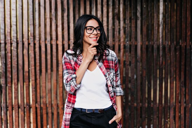 Menina pensativa, olhando para longe com um sorriso brincalhão. Mulher latina morena de óculos pensando em algo agradável.