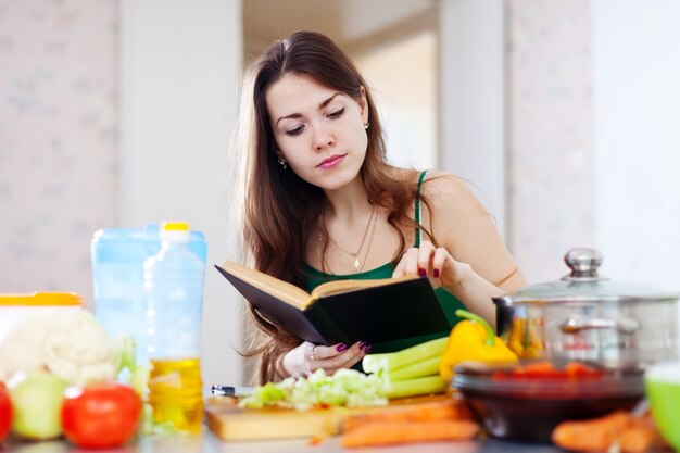 Menina pensativa que cozinha com livro de receitas