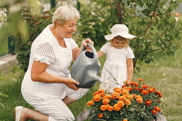 Menina pequena com avó sênior de jardinagem no jardim do quintal. Criança com um chapéu branco.