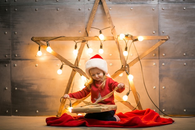 Menina pequena com presentes no Natal sentado no cobertor vermelho pela estrela