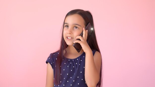 Menina pré-escolar em um vestido segurando um telefone celular, isolado sobre rosa