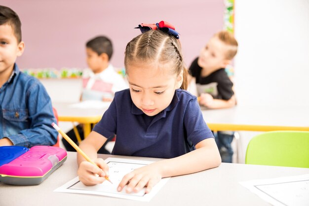 Menina pré-escolar ocupada fazendo alguns exercícios de matemática em uma sala de aula