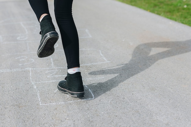 Menina pulando em caixas de giz desenhadas no asfalto