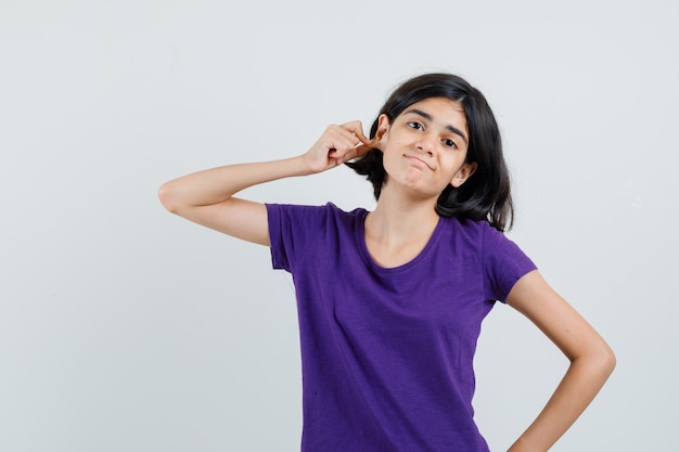 Menina puxando o lóbulo da orelha para baixo com uma camiseta e parecendo confusa