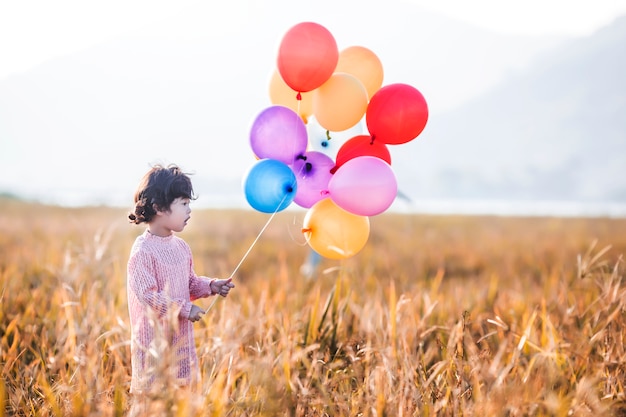 Menina que joga com os balões no campo de trigo