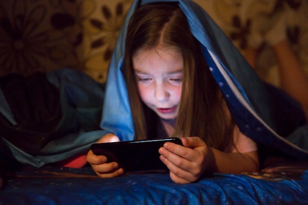 Foto grátis menina que joga o jogo do smartphone no quarto escuro