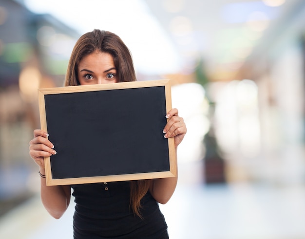 Foto grátis menina que mostra um pequeno quadro-negro com fundo borrado