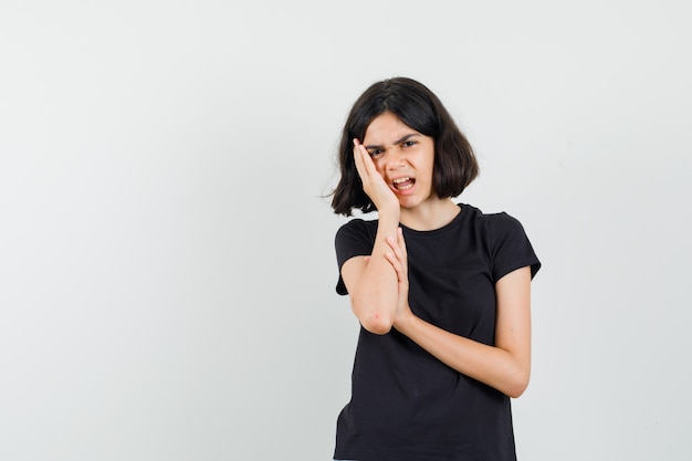 Menina que sofre de dor de dente em uma camiseta preta e parece irritada. vista frontal.