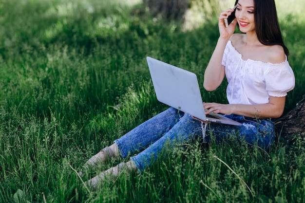 Menina que sorri ao falar no telefone e ter um laptop