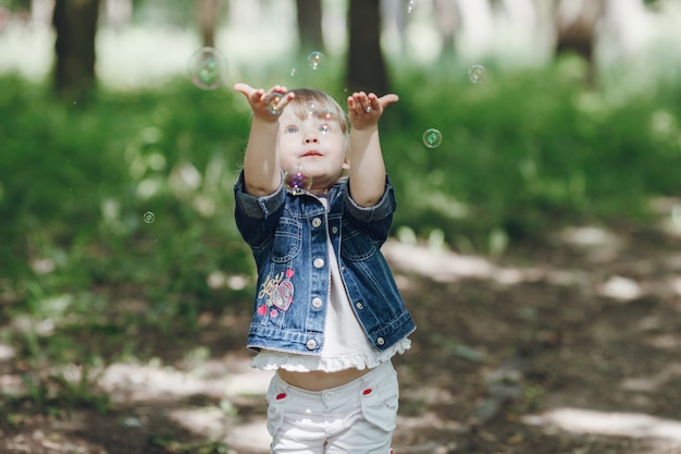 Menina que tem o divertimento com bolhas de sabão no parque