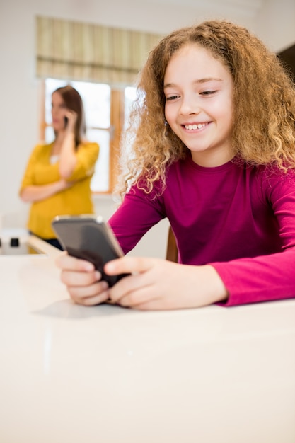 Menina que usa o telefone móvel na cozinha