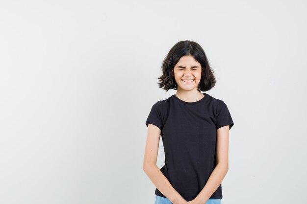 Menina rindo em t-shirt preta, shorts e parecendo feliz, vista frontal.