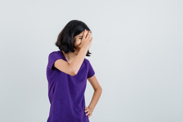 Menina rindo por trás da mão em uma camiseta e parecendo brincalhão.