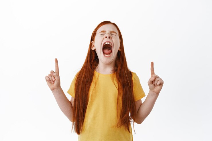 Foto grátis menina ruiva gritando e apontando os dedos para cima ginger kid com sardas gritando e mostrando algo de lado no fundo branco do espaço de cópia