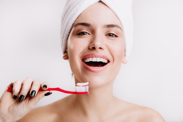 Menina saudável positiva faz tratamentos matinais para beleza e higiene. Mulher com toalha branca na cabeça, posando com escova de dentes.