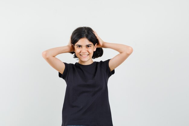 Menina segurando a cabeça com as mãos em uma camiseta preta e parecendo feliz. vista frontal.