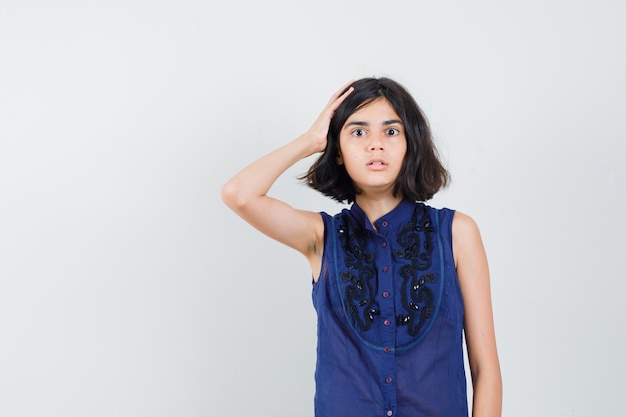 Menina segurando a mão na cabeça com blusa azul e parecendo confusa. vista frontal.