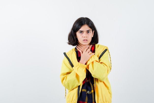 Menina segurando a mão na garganta com uma camisa xadrez, jaqueta e parecendo doente