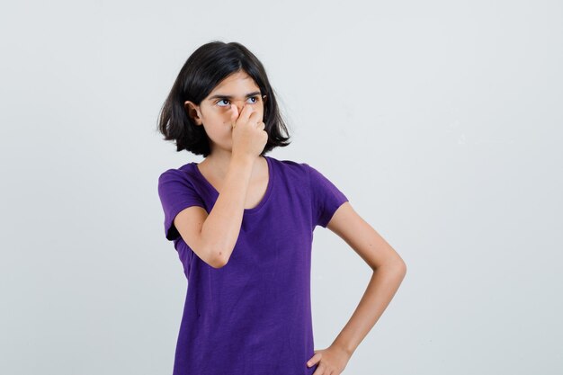 Menina segurando a mão no nariz em uma camiseta e parecendo pensativa,