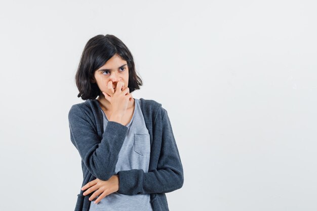 Menina segurando a mão no queixo com camiseta, jaqueta e parecendo pensativa