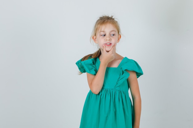 Menina segurando a mão no queixo com um vestido verde e bonita. vista frontal.