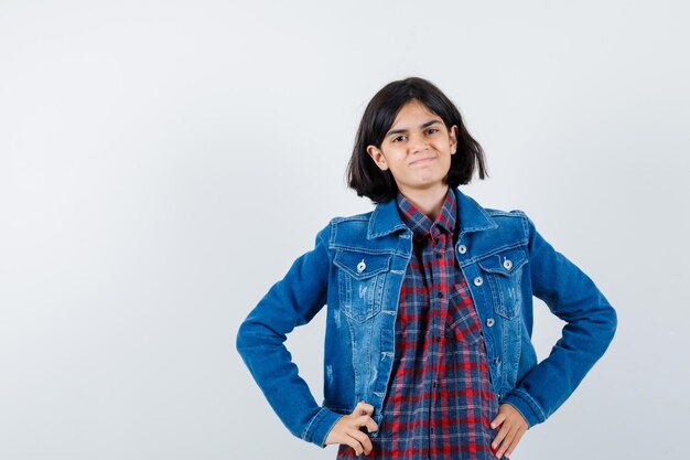 Menina segurando as mãos na cintura em uma camisa, jaqueta e parecendo alegre. vista frontal.