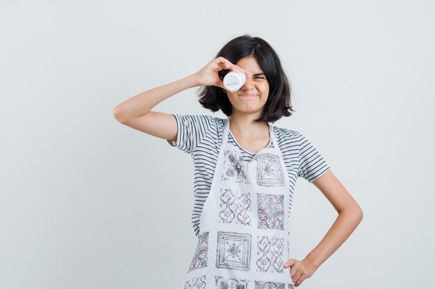 Menina segurando o frasco de comprimidos na camiseta, avental e parecendo brincalhona,