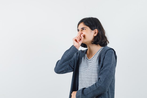 Menina segurando o punho no queixo com camiseta, jaqueta e parecendo sonhadora