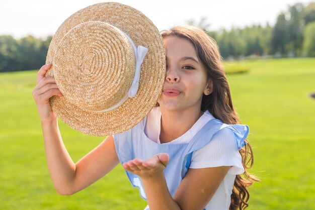 Menina segurando um chapéu enquanto sopra beijos