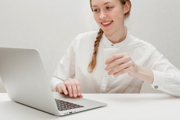 Menina segurando um copo de leite enquanto olha no seu laptop