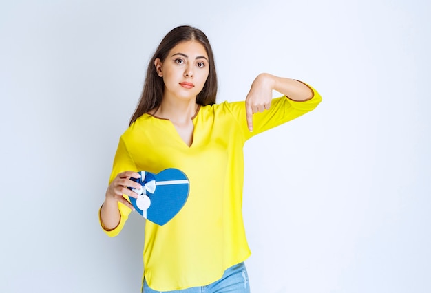 Menina segurando uma caixa de presente da forma de coração azul e chamando alguém para apresentá-la.