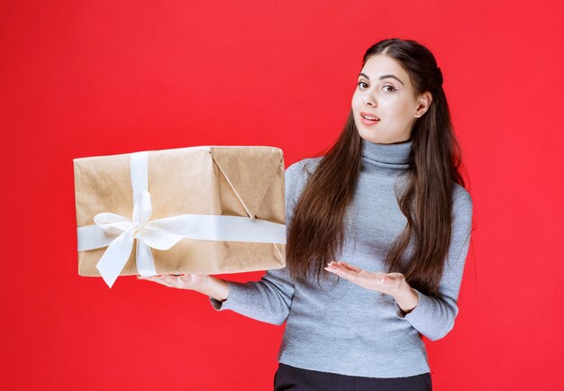 Menina segurando uma caixa de presente de papelão e apontando para ela.